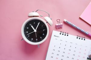 An image of a white clock and calendar on a pink background